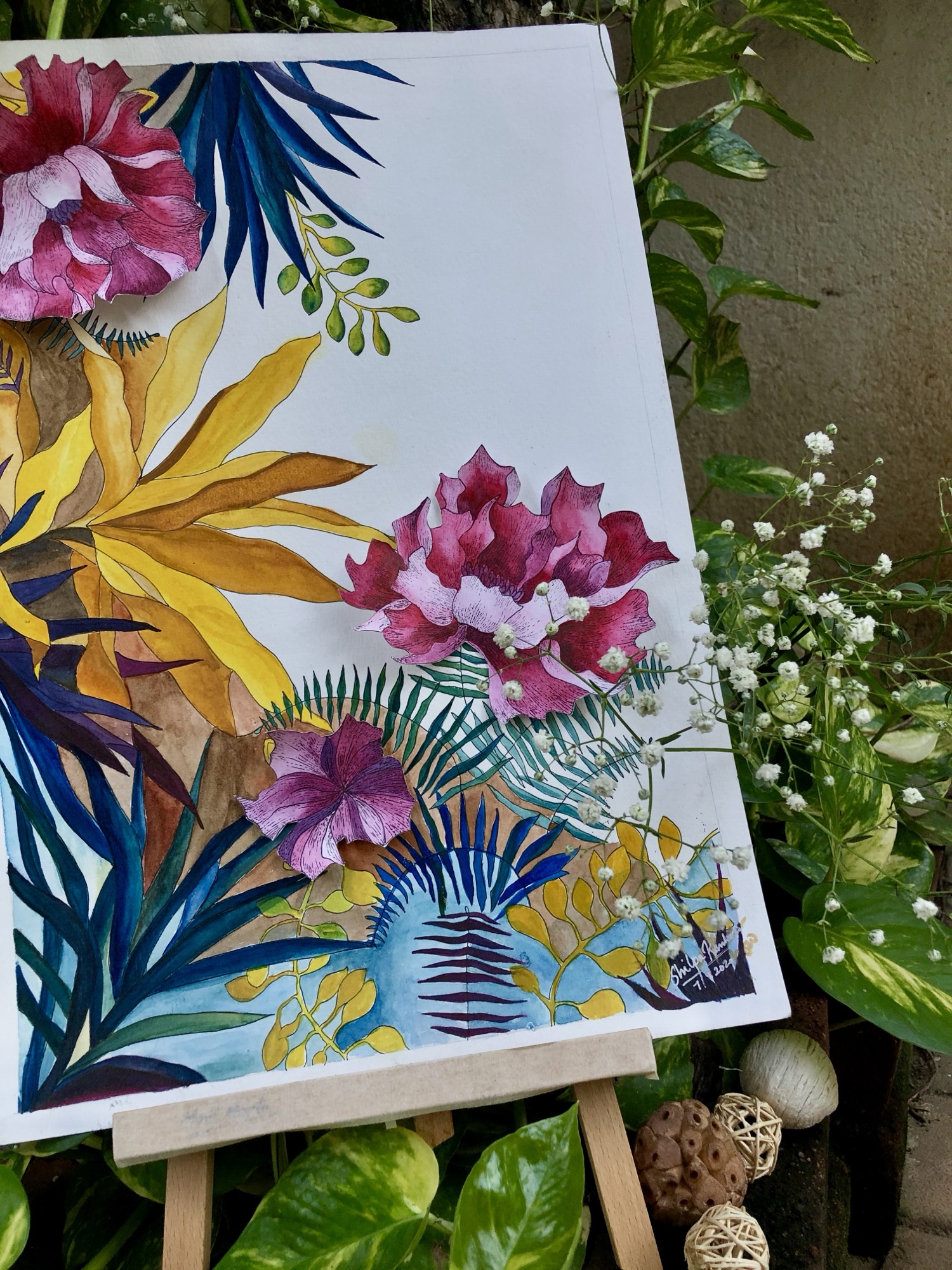 Watercolour painting of pink bougainvillea, yellow bird-of-paradise and ferns, propped on an easel outdoors