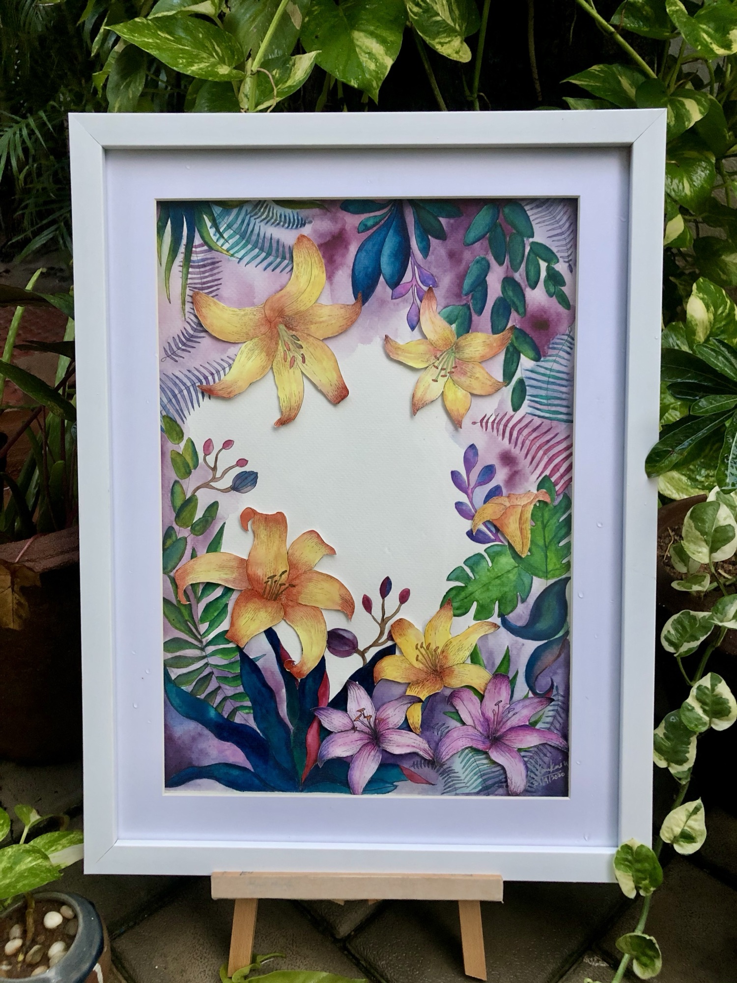 Framed watercolour painting of yellow lilies and purple florals arranged in a circular wreath